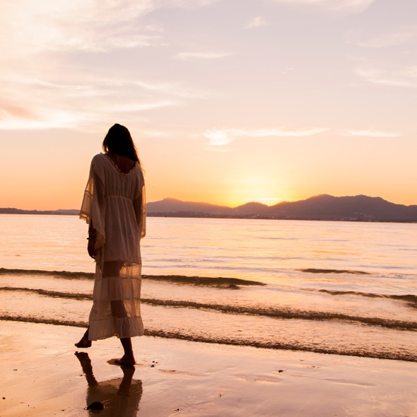 Woman walking along a beach at sunset